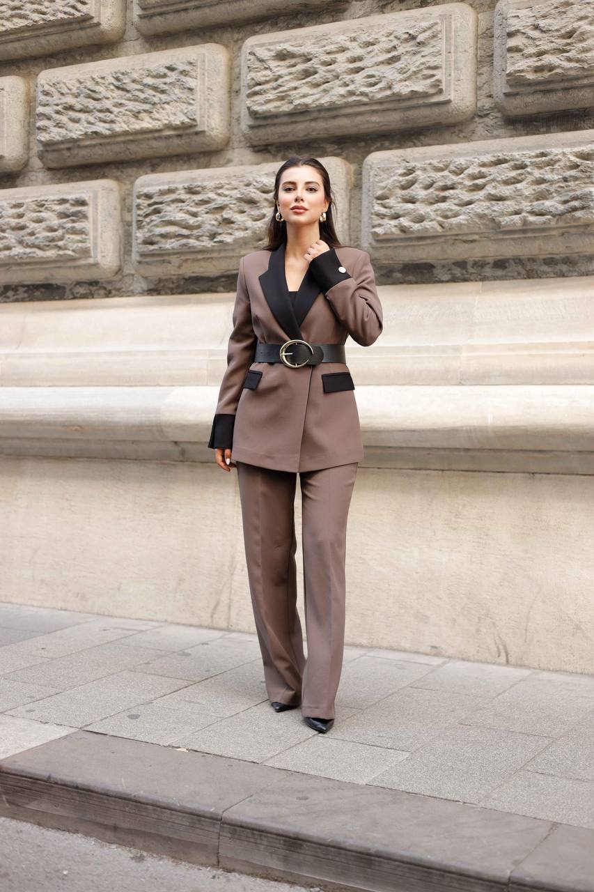 Woman in a brown suit standing against a stone wall.