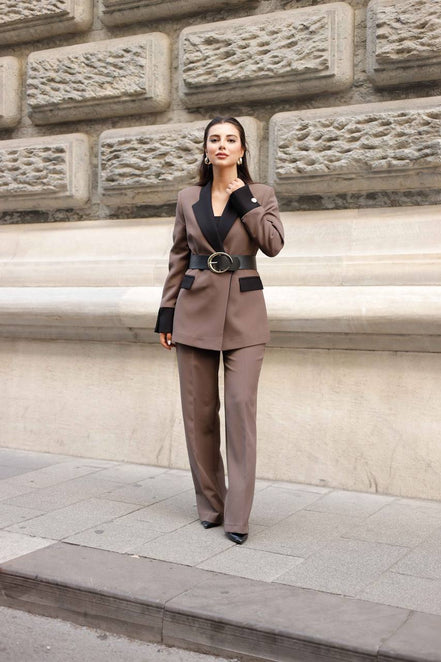 Woman in a brown suit standing against a stone wall.